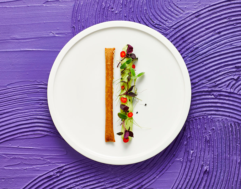 Een mooi strak hapje, bestaande uit een kant-en-klare vega-snack geflankeerd door een huisgemaakte acovadocrème, besprenkeld met kleurrijke cressen en pepers. 