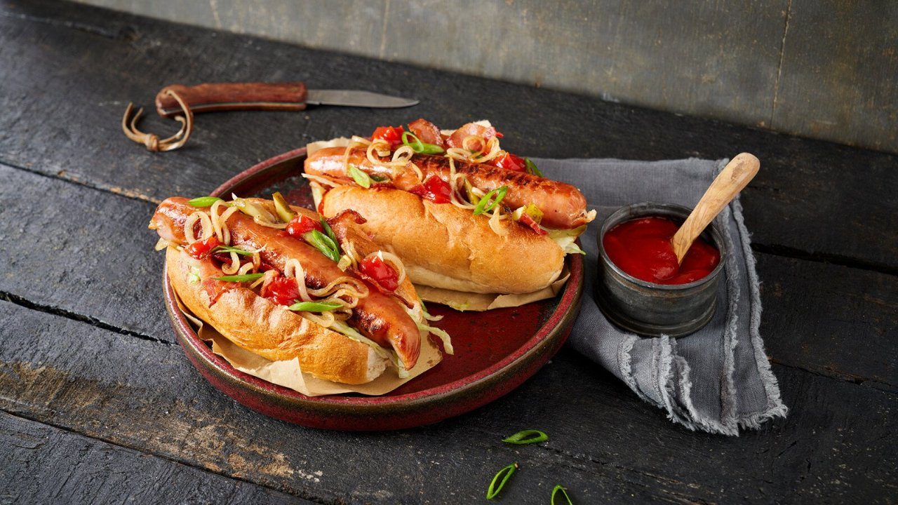 Een heerlijke hotdog American Style! Bereid met bacon, ijsbergsla, zoete ui en de nieuwe Remia Rebel Red American Ketchup.